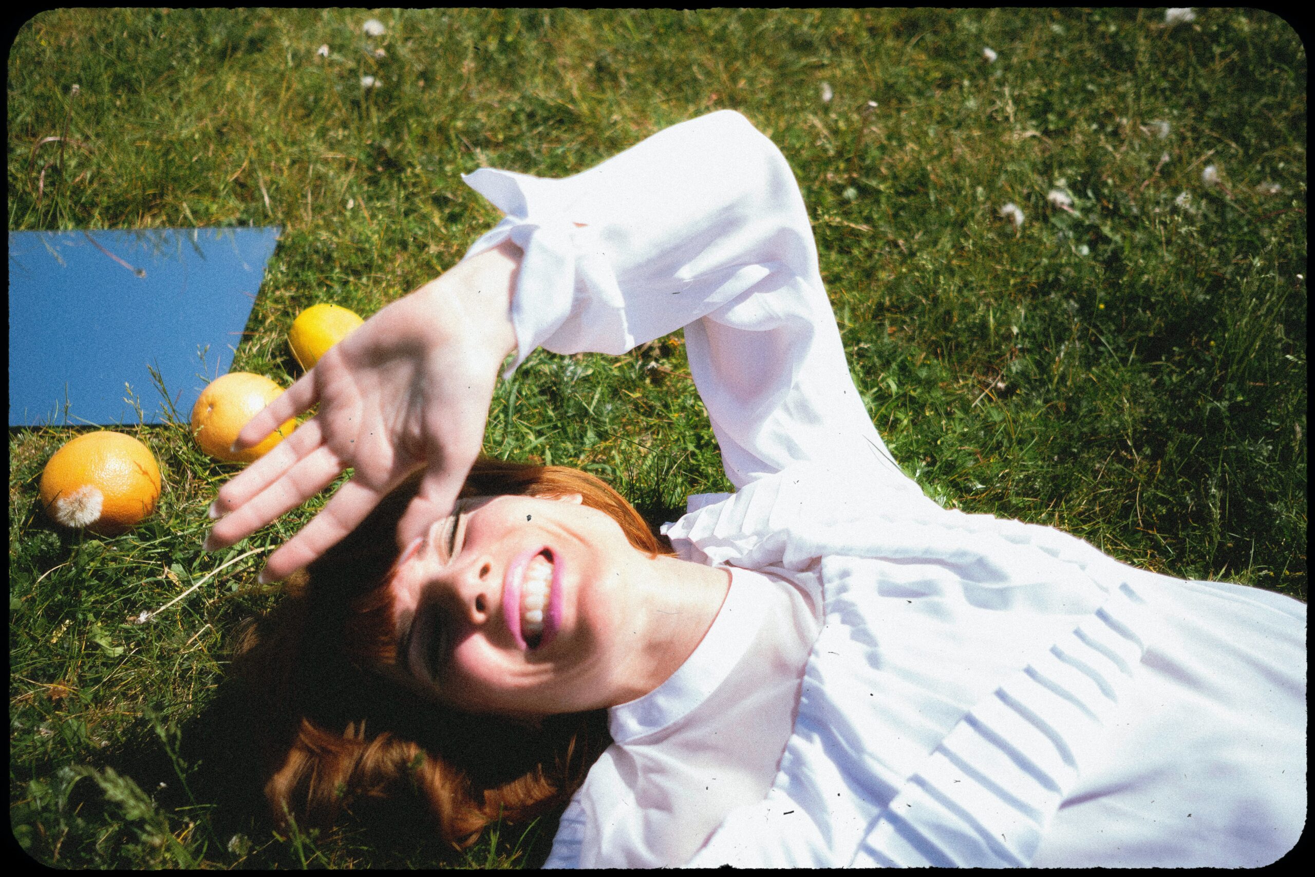 A woman smiling in the grass blocking her face from a Rosacea Trigger, sunlight.